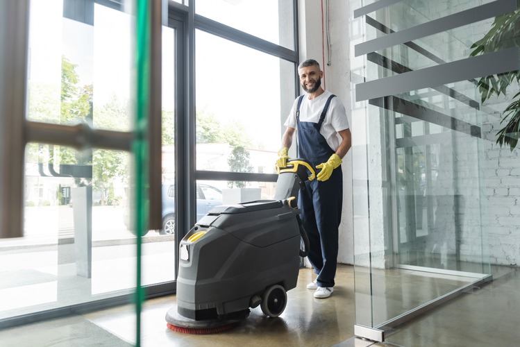 operario limpiando de pie con una maquina fregadora automática el hall de un edificio o instalación.